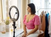 Young woman in pink top setting up camera for video recording with ring light indoors.