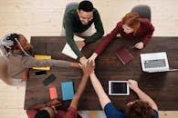 Top view of a diverse team stacking hands in unity over a wooden table, displaying teamwork.